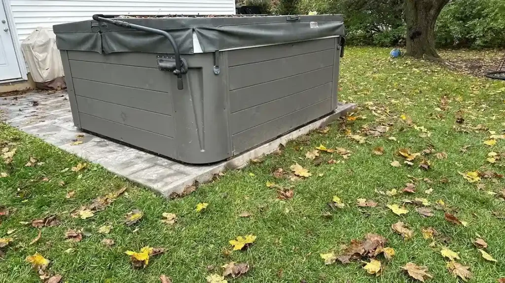 Above-ground hot tub with closed cover on a paver base surrounded by fall leaves in a residential backyard in Lakehurst, NJ by Gorlin Pools