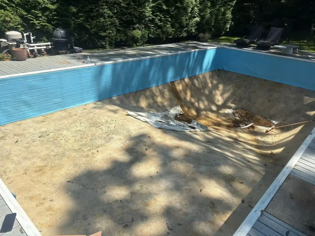 Drained pool with blue foam insulation panels installed on walls and old liner remnants on the sand floor during renovation in Lakehurst, NJ by Gorlin Pools