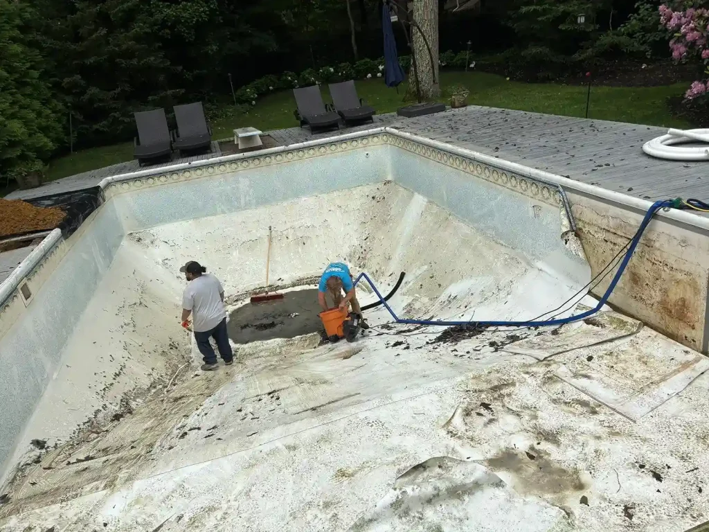 Two Gorlin Pools crew members removing a worn and damaged vinyl liner from an empty pool in Lakehurst, NJ