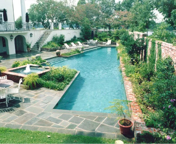Lap pool with a square fountain feature, brick retaining wall, and bluestone patio at a Mediterranean-style estate in Lakehurst, NJ by Gorlin Pools