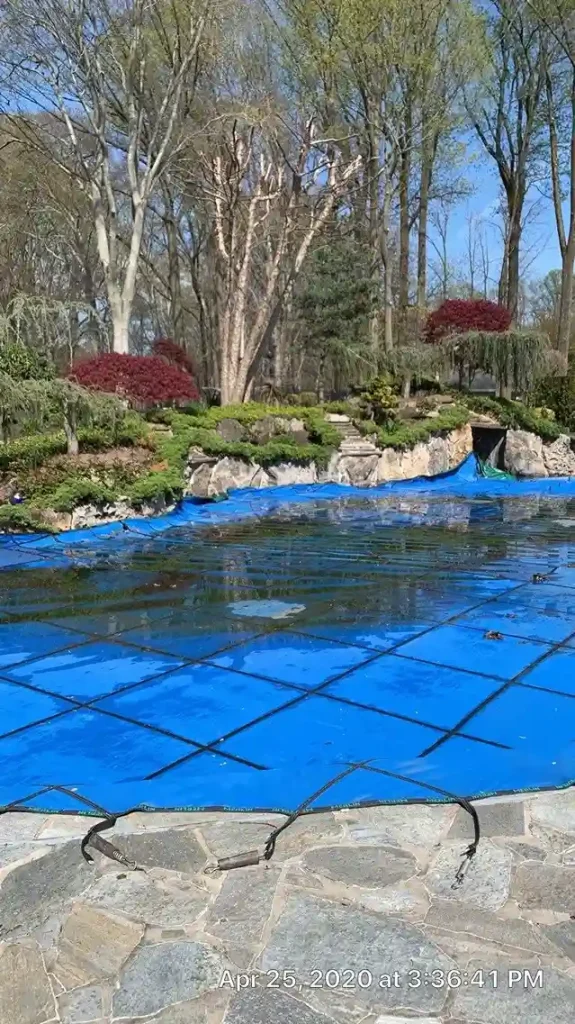 In-ground pool with blue mesh safety cover ready for spring opening on a flagstone patio in New Jersey by Gorlin Pools