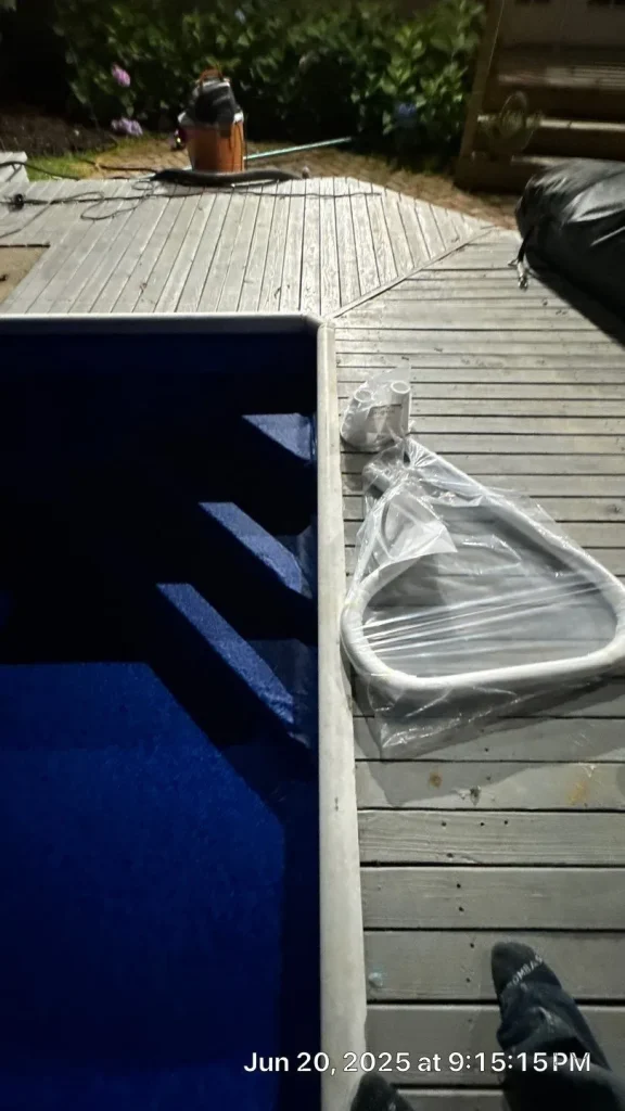 Pool skimmer net and new fittings laid out on a wood deck beside a freshly lined pool during a nighttime installation in Lakehurst, NJ by Gorlin Pools