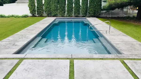 Rectangular fiberglass pool with gray finish, stainless steel handrail, and concrete paver surround with grass strips in Lakehurst, NJ by Gorlin Pools