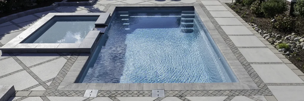 Rectangular gunite pool with attached square spa, built-in steps, and decorative mosaic paver border patio in Lakehurst, NJ by Gorlin Pools